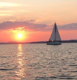 Sunset over water with sailboat in silhouette